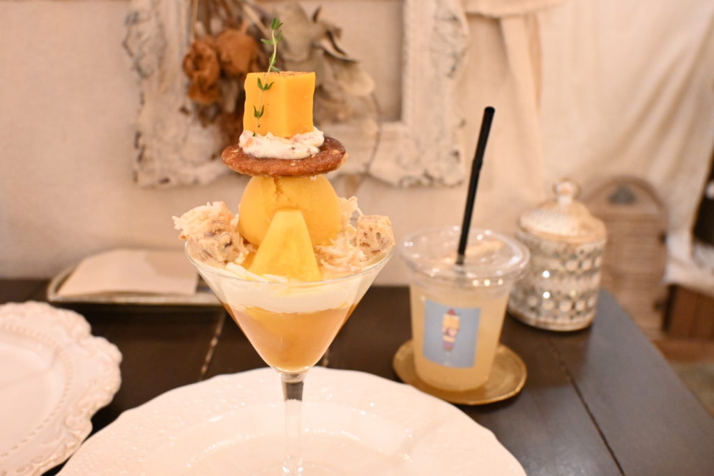 カクテルグラスに盛り付けられたマンゴーとパインの贅沢トロピカルパフェ。アンティーク調カフェで味わえるフォトジェニックなスイーツ。