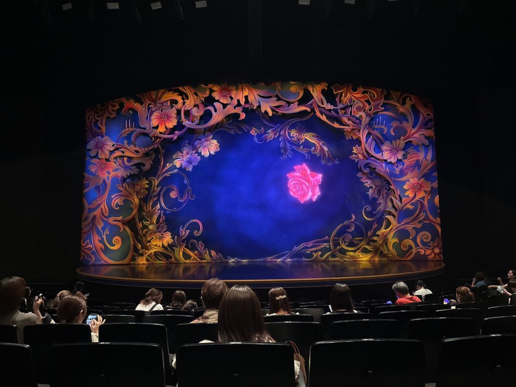 開演前の舞台を座席から撮影。幻想的なバラが描かれた美しい緞帳と、静かに開演を待つ観客たちの様子。