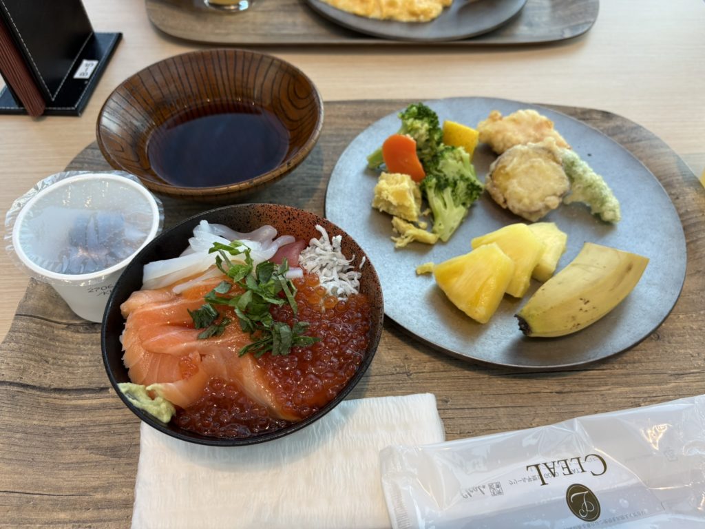 木製のトレーに置かれた、いくらやサーモンなどがのった海鮮丼と、天ぷらやフルーツが盛られたプレート